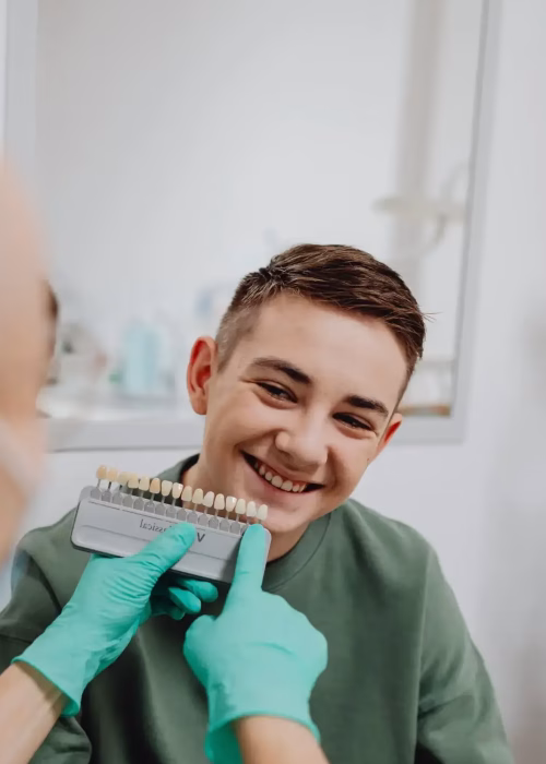 A smiling teenager having his tooth shade measured by a dental professional to ensure a seamless composite restoration match.