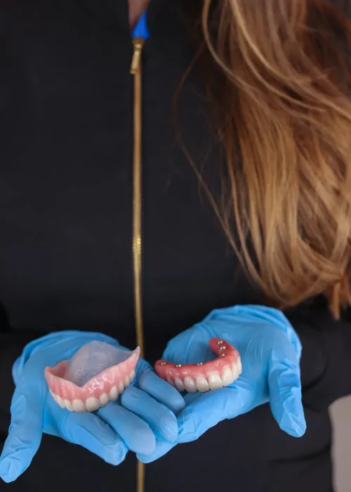 A dental professional wearing blue gloves and holding a custom complete upper and lower denture set.